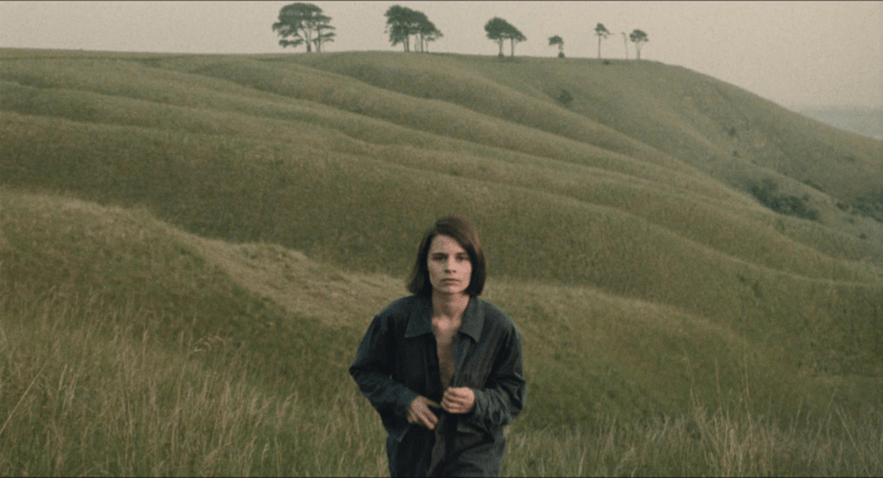 A woman in a mostly unbuttoned shirt against a vast, grassy landscape